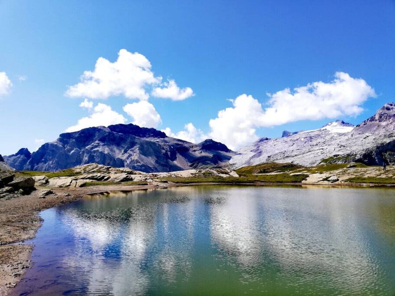 A mountain landscape with a clear lake, rocky terrain, and snow-capped peaks.