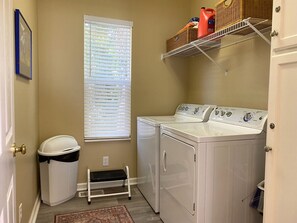A laundry room with a washing machine, dryer, and a shelf with laundry supplies.