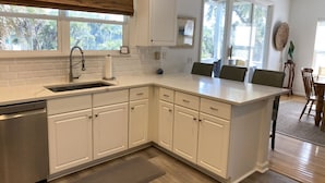 A modern kitchen with white cabinetry, a stainless steel dishwasher, and a large island with seating.