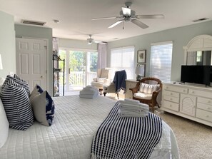 Un dormitorio con cama, una silla, televisor y balcón.