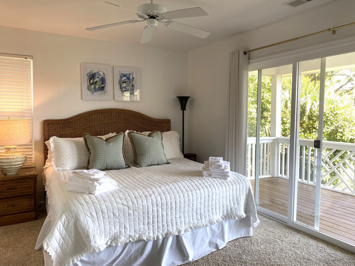 Ein Schlafzimmer mit einem großen Bett, einem Deckenventilator und Blick auf einen Balkon.