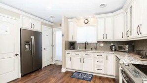 A modern kitchen with white cabinets, stainless steel appliances, and a wooden floor.