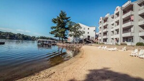 A beach with a row of white buildings, some with balconies, and a clear blue sky.