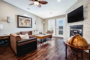 Relax in this inviting living room with a sofa, ottoman, and coffee table, featuring a large window with a view and a fireplace.