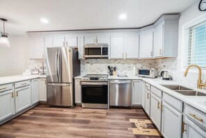 Een moderne keuken met witte kasten, roestvrijstalen apparatuur en een houten vloer.