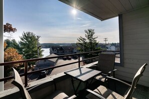 Balkon med et bord og stole, udsigt over en parkeringsplads og bygninger.