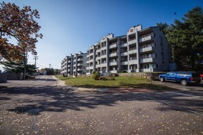 En flereretages boligbygning med altaner, parkeringsplads og en klar himmel.