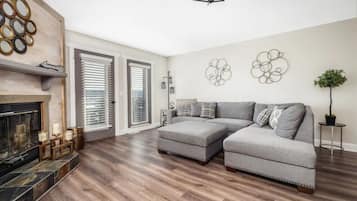 Ein modernes Wohnzimmer mit einem Ecksofa, einem Kamin und einem großen Fenster mit Jalousien.
