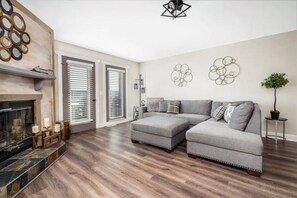Een moderne woonkamer met een modulaire bank, een open haard en een groot raam met zonwering.