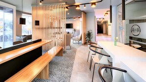 A modern hotel lobby with a reception desk, seating area, and a large window offering a view of the street. - B&B Hotel Bochum-City (Bochum)