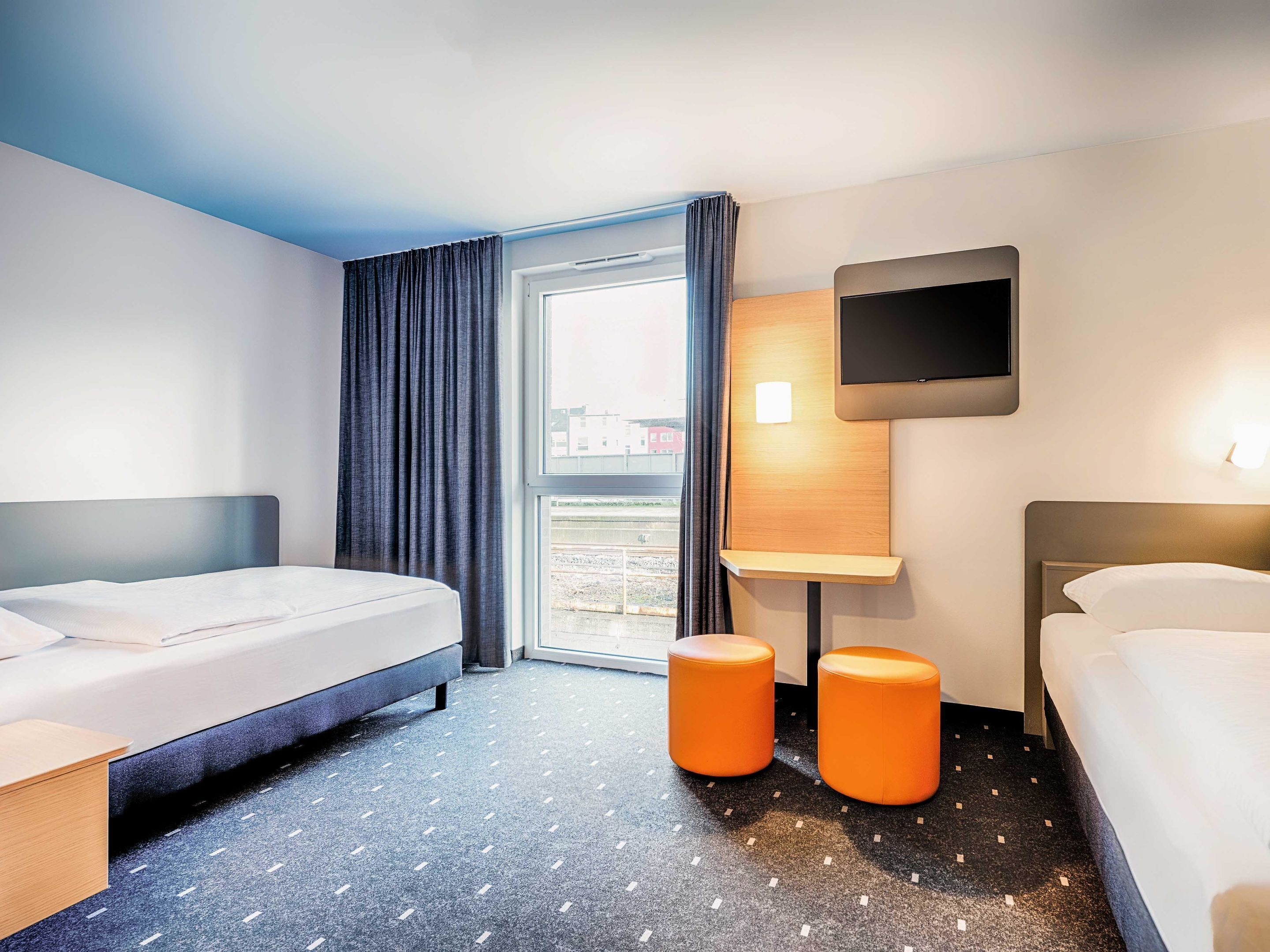 Habitación de hotel con dos camas, televisión y ventana con cortinas.