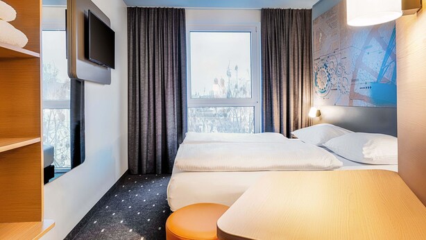 Una habitación de hotel con dos camas, televisión, ventana con cortinas, un cuadro de un mapa en la pared y una mesita.