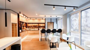 A modern cafe with a long counter, black chairs, and a large window. - B&B Hotel Bochum-City (Bochum)