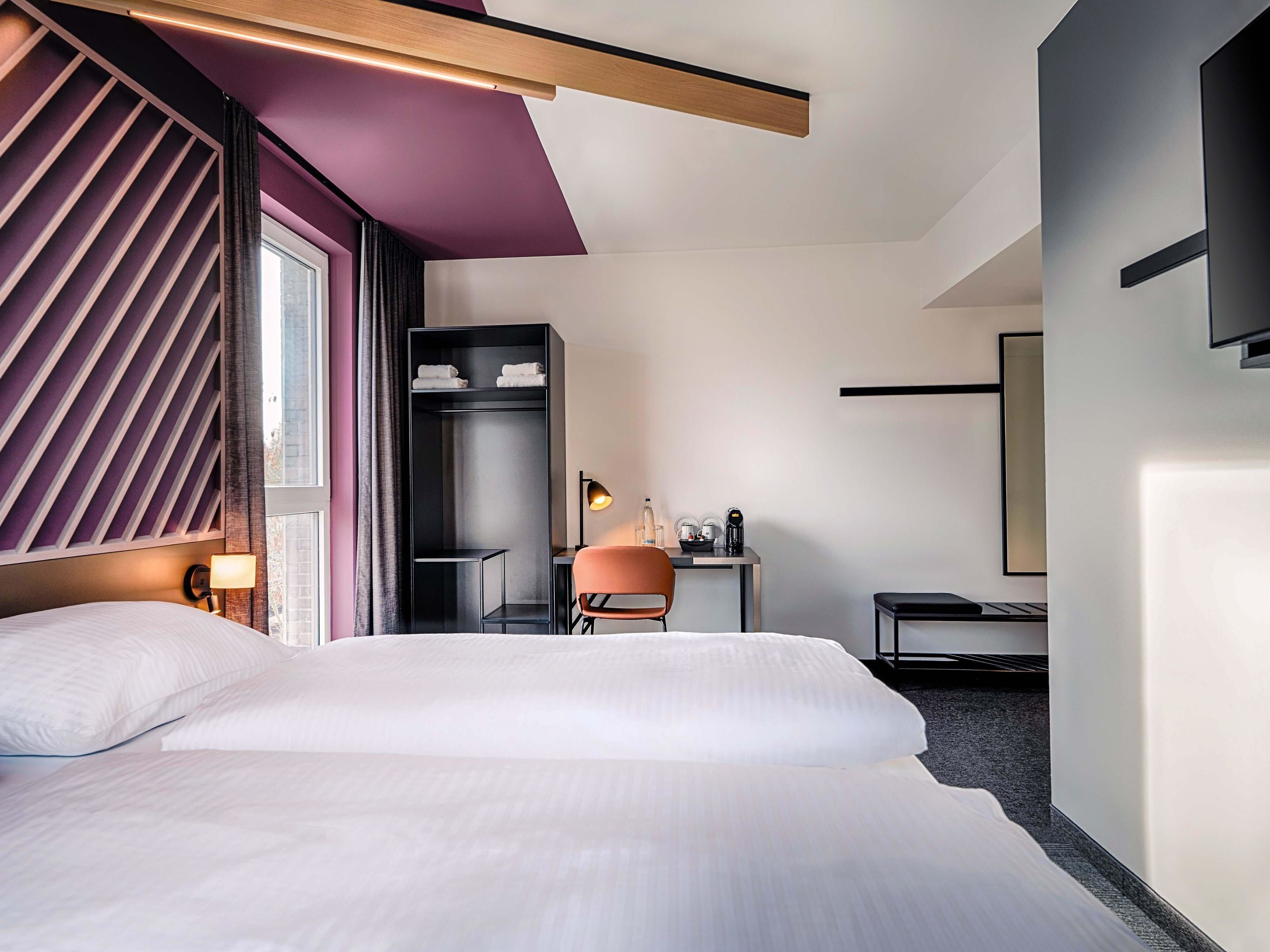Una habitación de hotel moderna con una cama grande, un escritorio con silla, un armario y un televisor de pantalla plana montado en la pared.