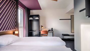 Ein modernes Hotelzimmer mit einem großen Bett, einem Schreibtisch mit Stuhl, einem Kleiderschrank und einem wandmontierten Flachbildfernseher.