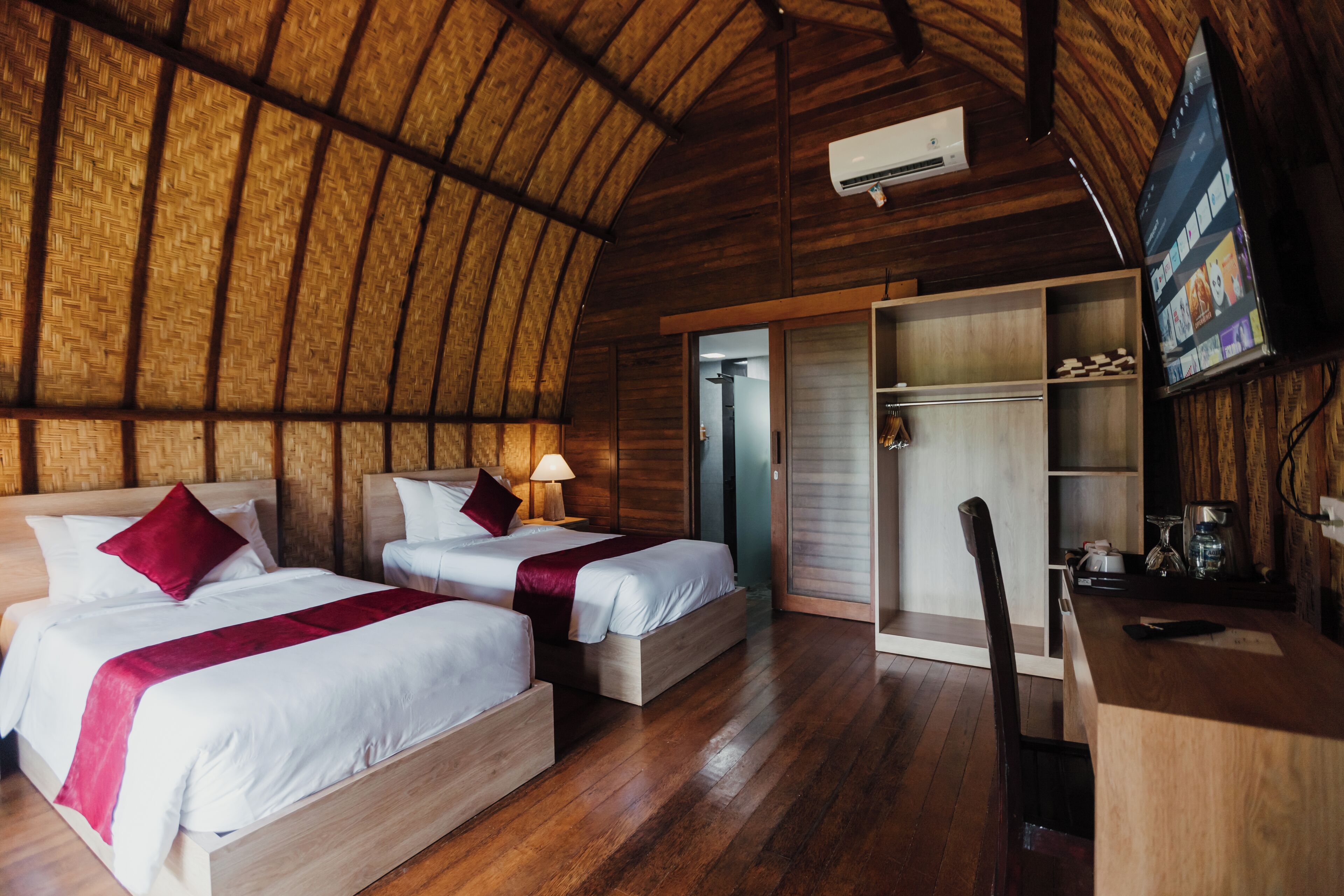 Una habitación con dos camas, suelo de madera, un armario y un televisor.