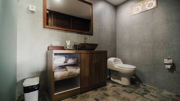 A bathroom with a wooden vanity, a white toilet, a large mirror, and a stone-patterned floor.