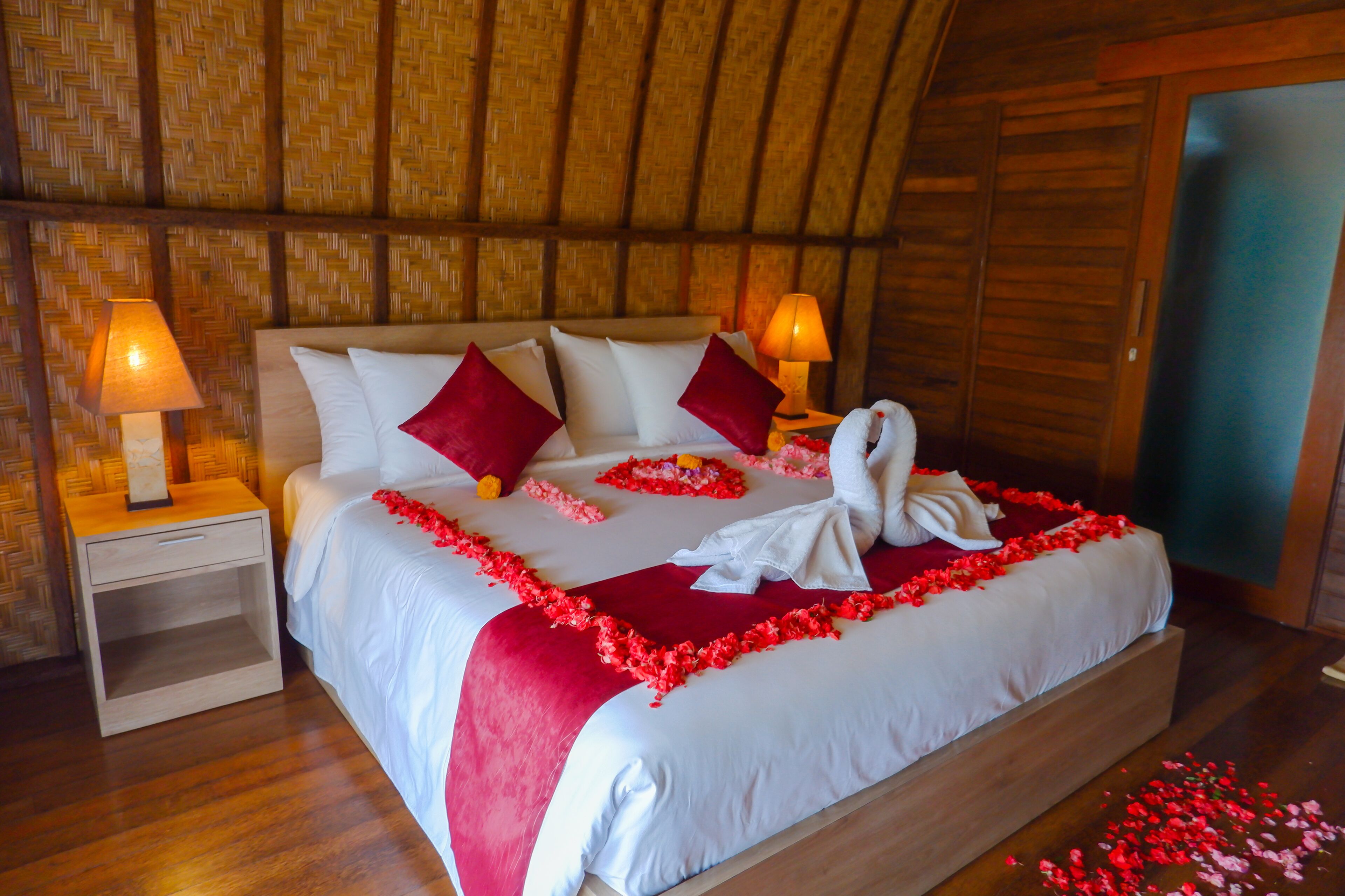 A bed with white linens, red pillows, and a red floral bedspread.