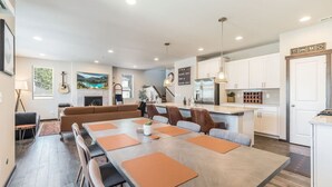 A modern kitchen with white cabinets, a dining area with a long table and orange placemats, and a cozy seating area with a brown sofa. - Impeccable 4 BR Home in Heart of Port Orchard (Port Orchard)
