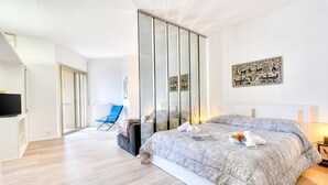 Habitació d'hotel moderna amb un llit gran, una televisió, una porta corredissa de vidre i una cadira blava.