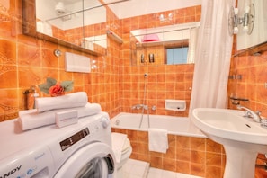 A bathroom with orange patterned tiles, a white sink, a bathtub, a mirror, and a washing machine. - Casa Emma With Sea Glimpse (Sanremo)