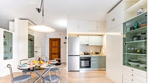 Una cuina moderna amb zona de menjador, electrodomèstics d'acer inoxidable i armaris amb portes de vidre.
