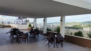 A covered outdoor seating area with chairs and tables, overlooking a cityscape with buildings and greenery. - Enjoy the luxury and comfort of living (Cebu)
