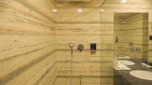 A bathroom with a marble wall, a glass-enclosed shower, and a sink with a mirror.