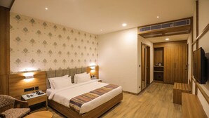 A hotel room with a bed, bedside table, chair, and a small table. There is a wardrobe and a television in the room.