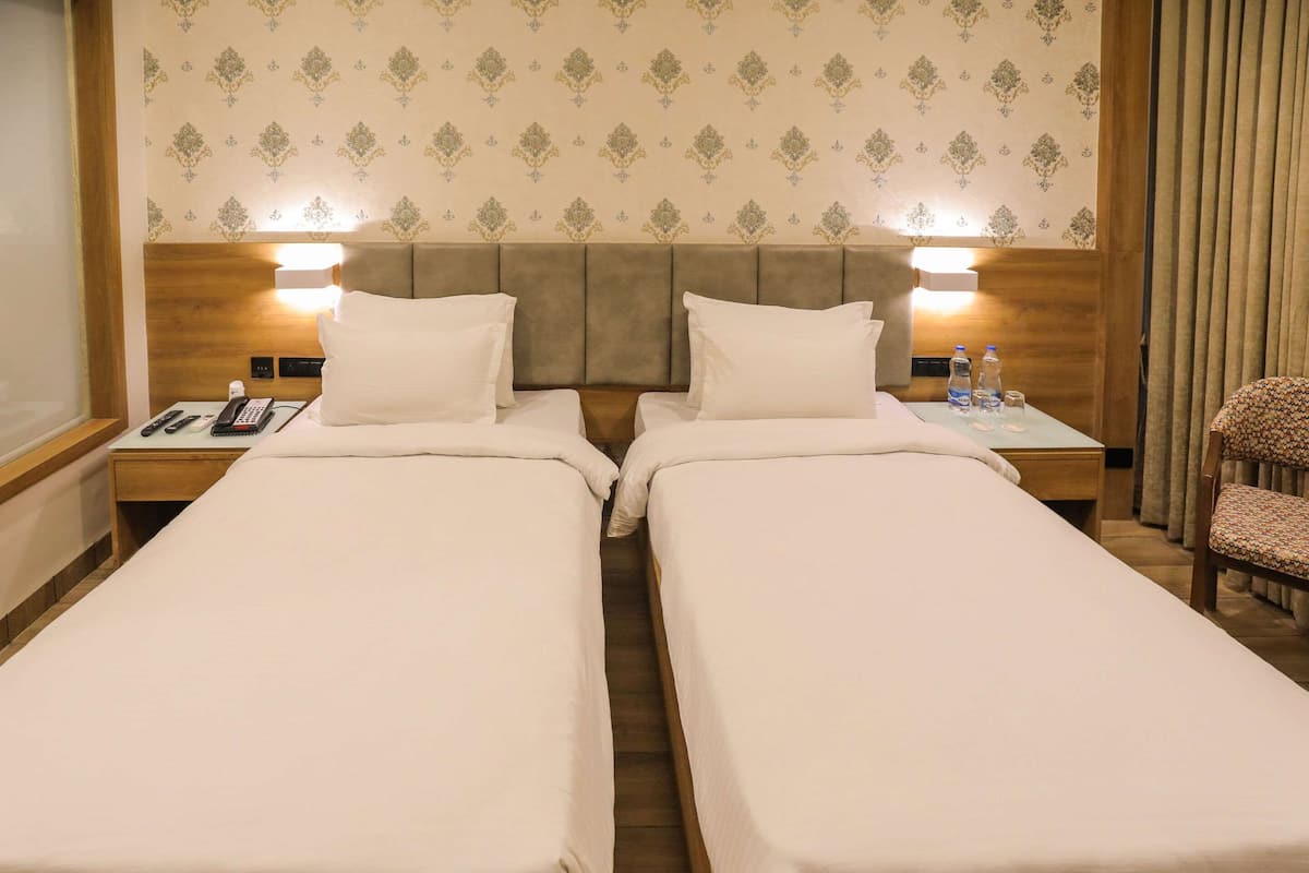 Habitación de hotel con dos camas individuales, mesitas de noche con lámparas, cabecera de madera y papel tapiz estampado.