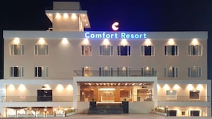 A multi-story hotel named "Comfort Resort" with a prominent sign, multiple balconies, and a well-lit entrance.