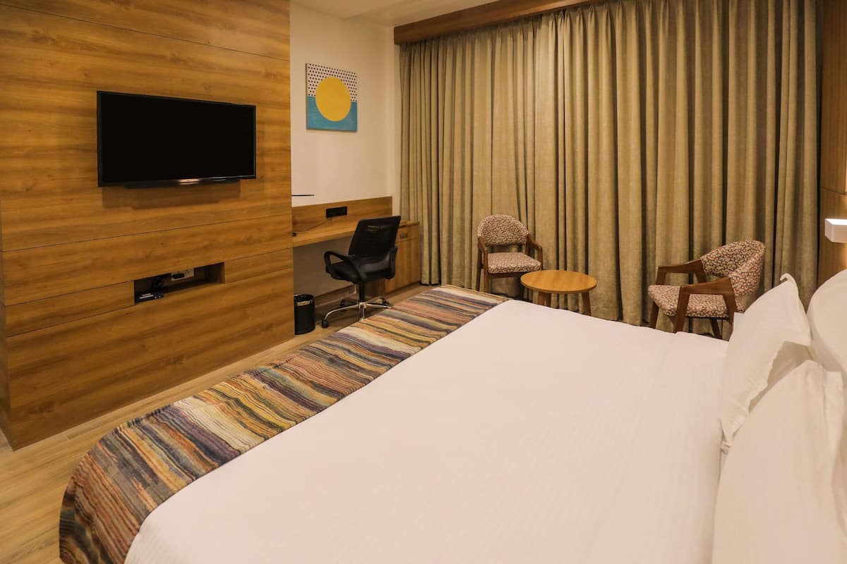 Habitación de hotel con una cama grande, un escritorio con silla, televisión montada en la pared y una ventana con cortinas.