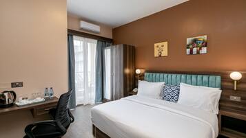 Habitación de hotel con una cama grande, un escritorio con silla, una ventana con cortinas y dos obras de arte en la pared.