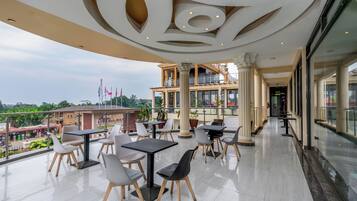 A spacious outdoor terrace with tables and chairs, a balcony with a view of the city, and a modern architectural ceiling design.