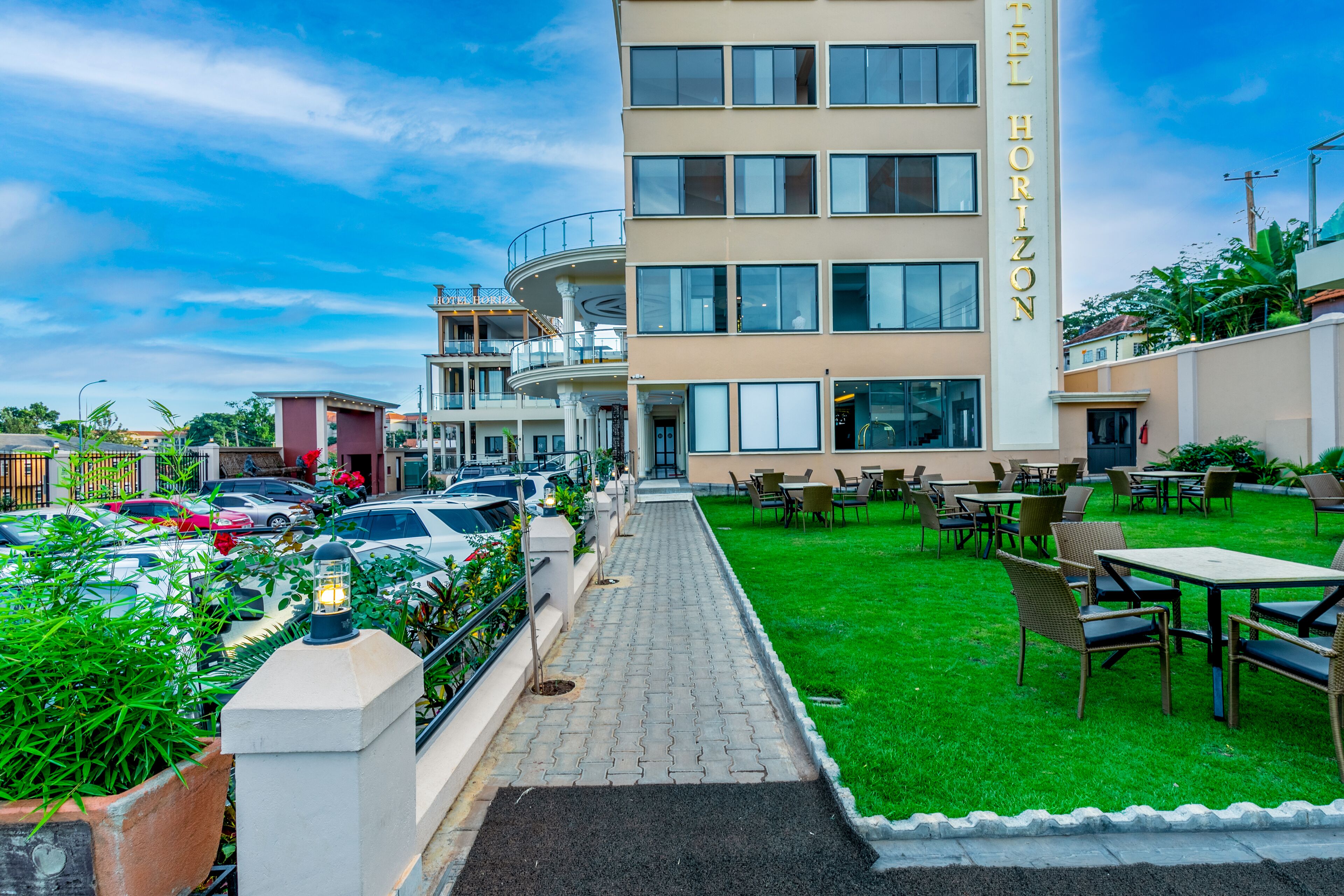 Un hotel con un camino pavimentado que conduce a un espacio al aire libre con césped, mesas y sillas.