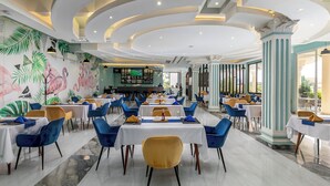 A restaurant with tables and chairs, a bar area, and a mural with tropical leaves and flamingos. - Hotel Horizon Entebbe (Entebbe)