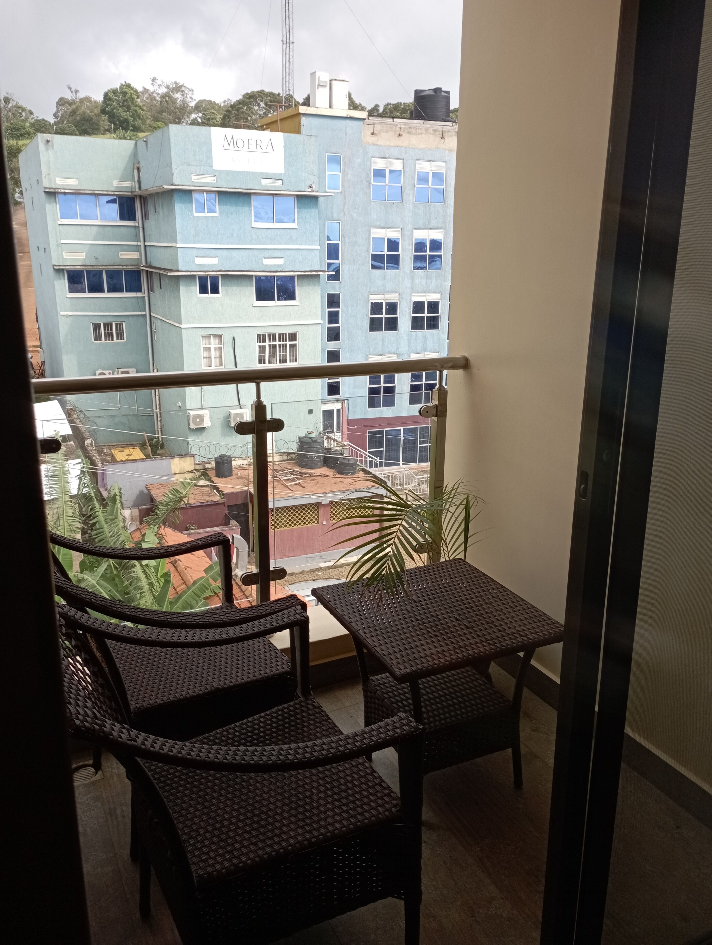 A balcony with wicker furniture, a view of a building labeled 'MOFRA,' and a clear sky.