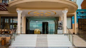 A grand entrance with a curved balcony, a staircase leading up to the entrance, and a clear view of the interior through the glass doors.