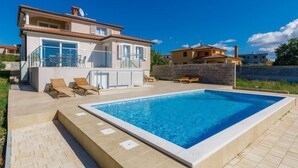 Ein modernes, zweistöckiges Haus mit Swimmingpool, Gartenmöbeln und blauem Himmel.