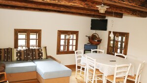 A cozy room with a wooden ceiling, a sofa, a dining table with chairs, and a television on the wall. - Tradicionalna Zagorska Drvena Kuća Stara Murva (Tuhelj)