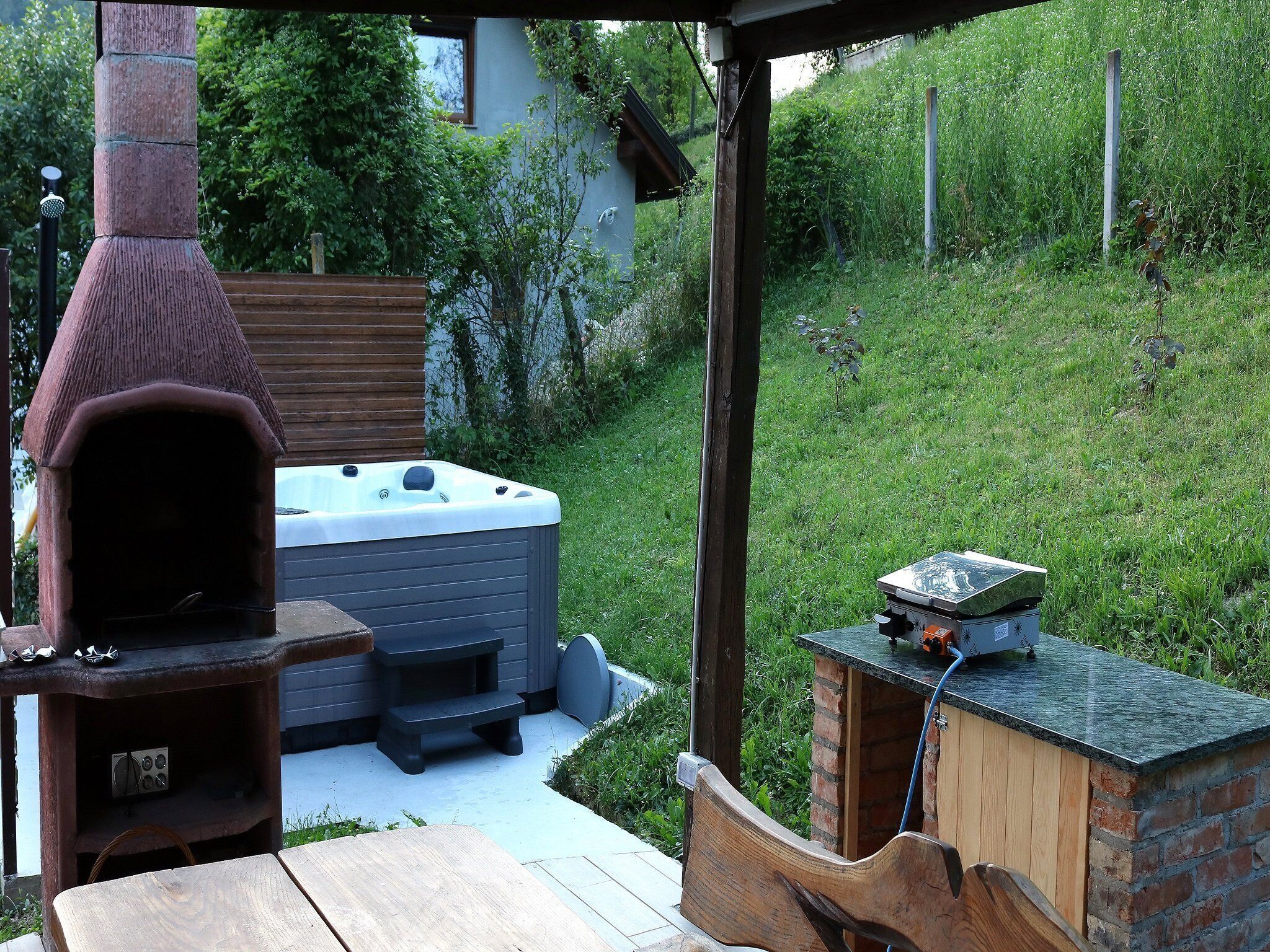 A backyard with a hot tub, a wooden table, and a brick barbecue grill.