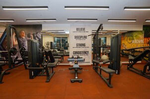 Un gimnasio con equipo de ejercicio variado, carteles motivacionales y un muro de espejos.