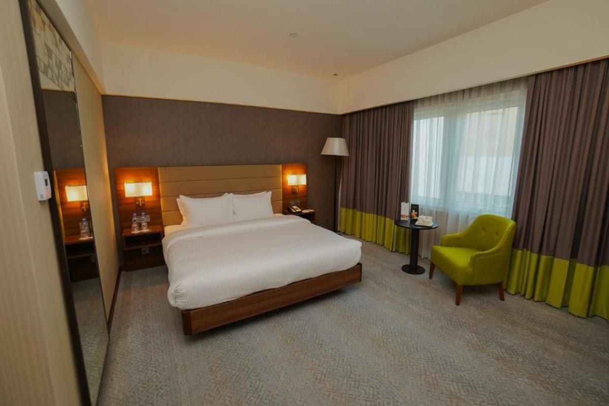 Une chambre d’hôtel avec un grand lit, des lampes de chevet, une petite table, une chaise et une fenêtre avec des rideaux.