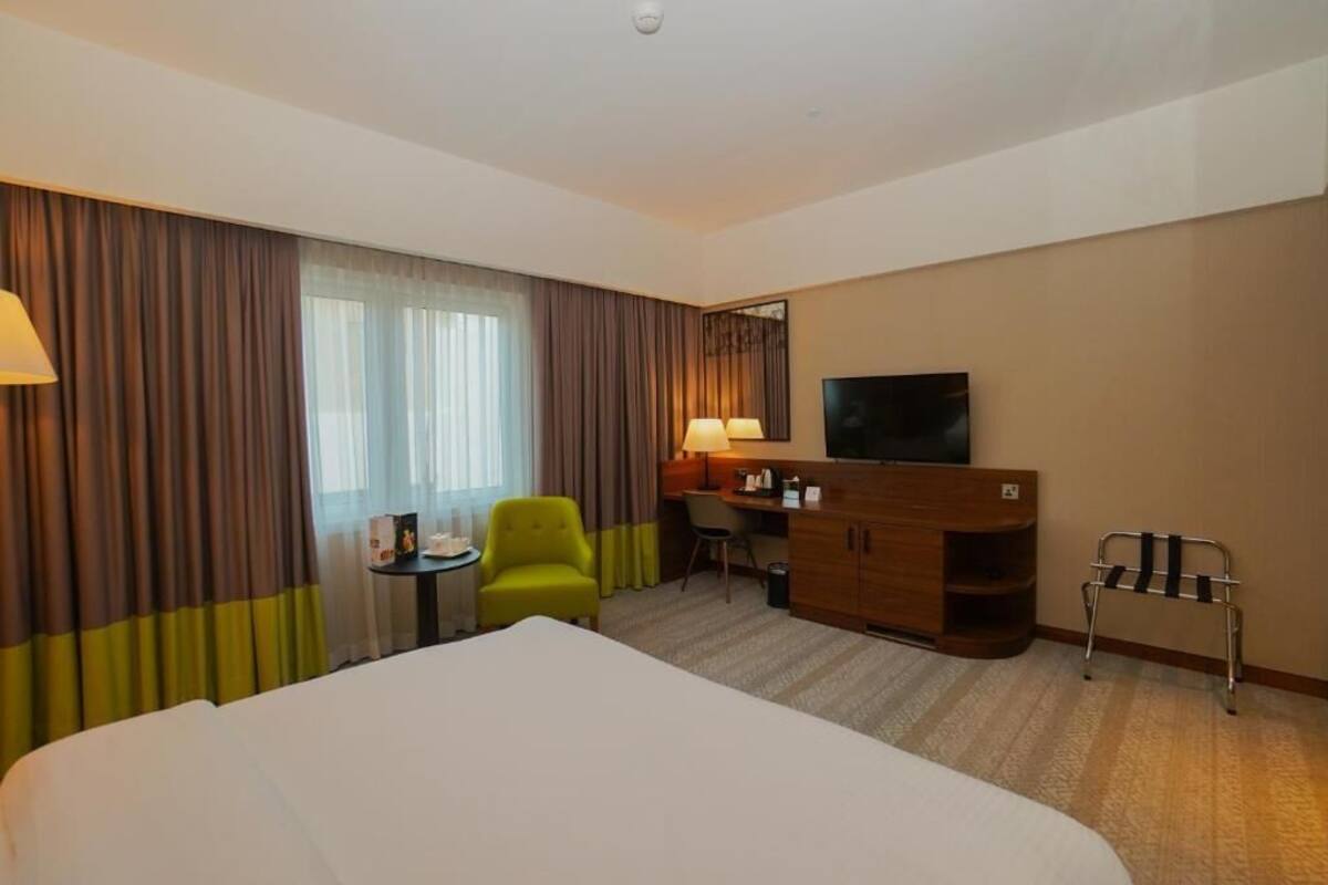 A hotel room with a bed, a desk, a chair, a TV, and a wheelchair.