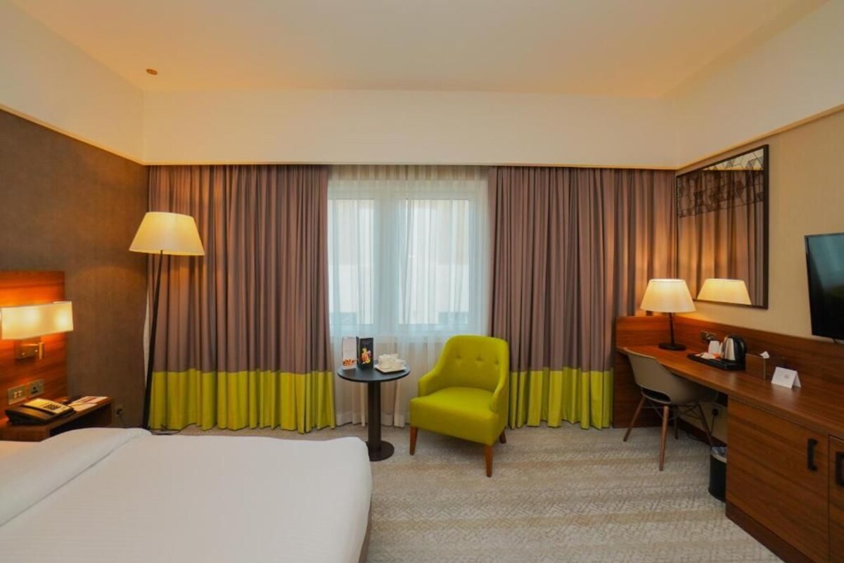 A hotel room with a bed, a desk, a chair, a small table, and a television.