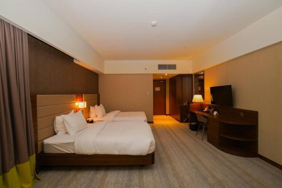 A hotel room with a bed, bedside lamps, a desk, a chair, and a television.