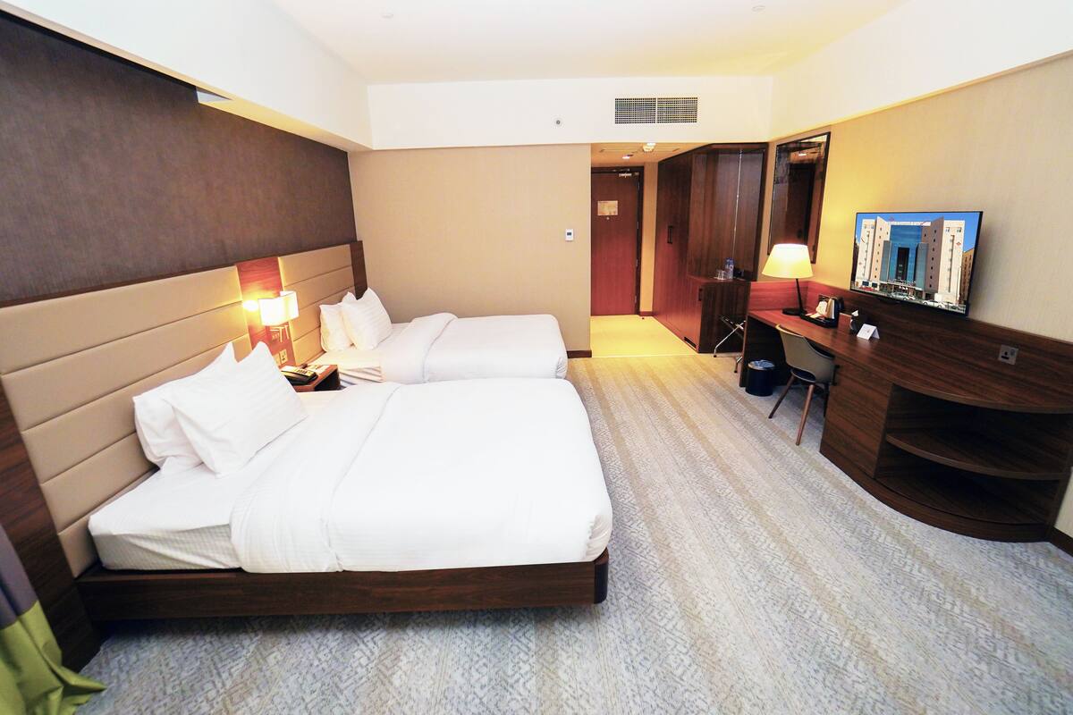 A hotel room with two beds, a desk, a chair, a mirror, and a television.