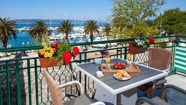 A terrace with a table set for breakfast, overlooking a marina with boats and palm trees. - Lux Apartment Mare By the Sea & Beach (Baska Voda)