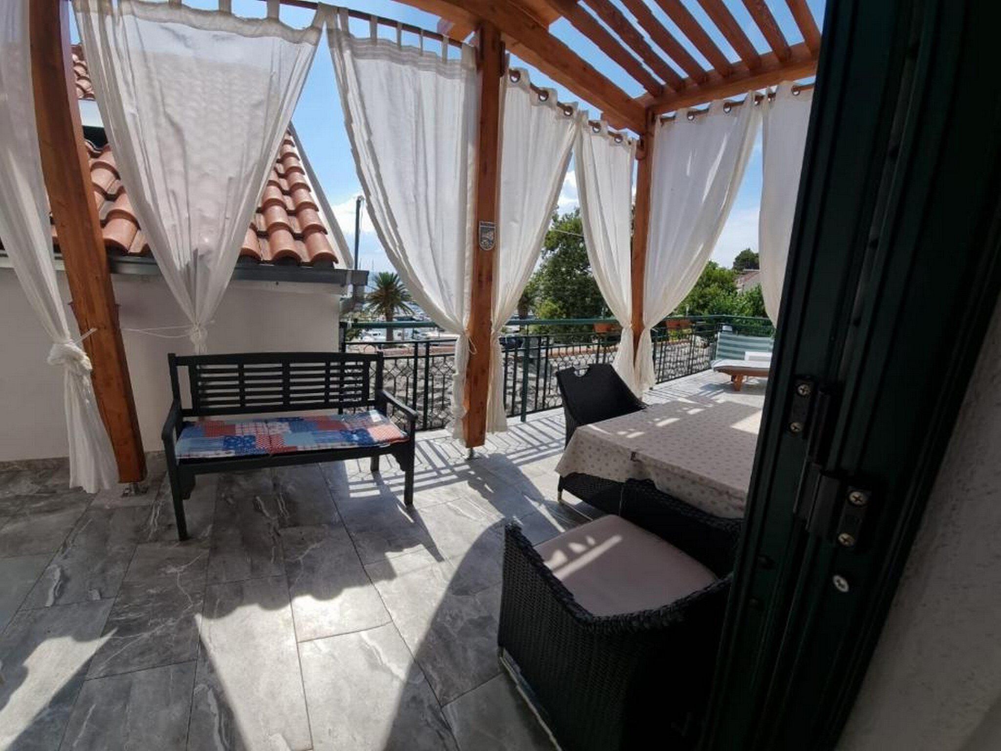 A covered outdoor seating area with a bench and a table, surrounded by white curtains.