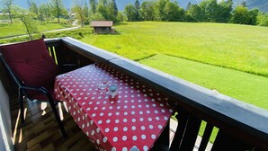 Un balcon avec une nappe à pois rouges, une chaise rouge et une vue sur un champ verdoyant, avec des arbres et une montagne en arrière-plan.